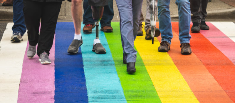 Menschen laufen über eine Straße, die in den Regenbogenfarben bemalt ist.